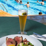 Copo em acrilico em primeiro plano e em segundo plano uma piscina com pessoas nadando.